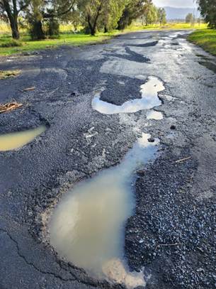 A road with potholes and water

AI-generated content may be incorrect.