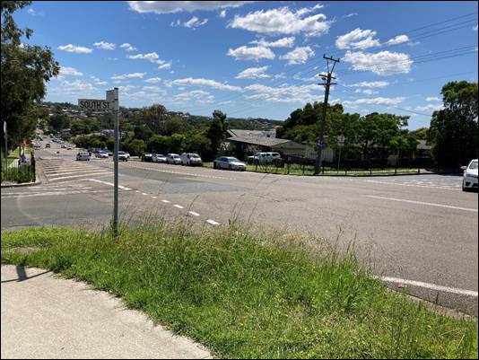 A road with grass and cars in the background

Description automatically generated